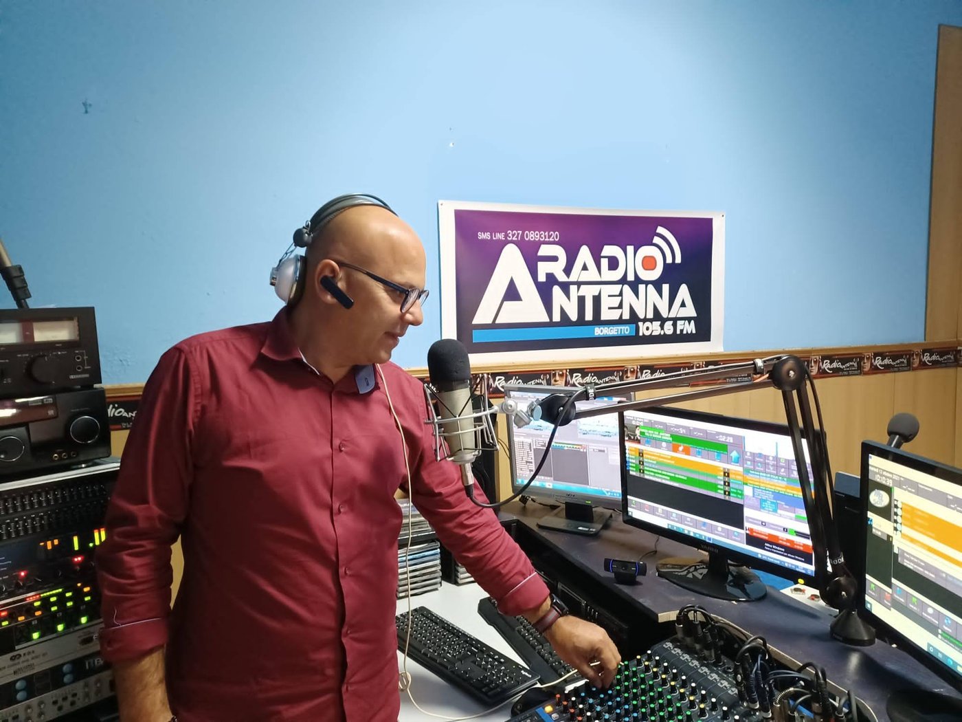 Lo studio digitalizzato di Radio Antenna, con la consolle, i monitor di regia e il poster storico Radio Antenna Borgetto 105.6 FM sullo sfondo